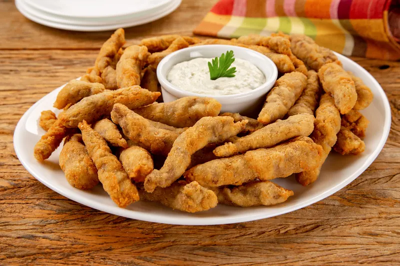 Tirinhas de frango empanadas com molho de gorgonzola, em travessa sobre mesa de madeira